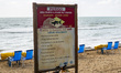 A warning sign about the danger of sharks is standing on the beach in the neighborhood of...
