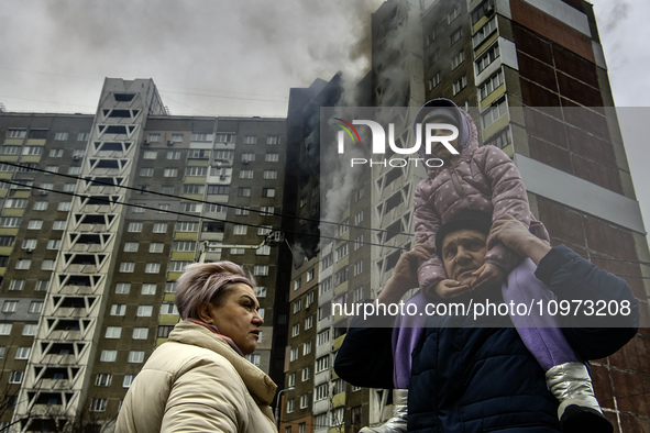 Local residents are watching as smoke rises from a burning residential high-rise building damaged by a massive Russian missile strike in Kyi...