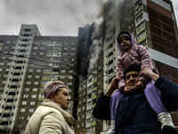 Local residents are watching as smoke rises from a burning residential high-rise building damaged by a massive Russian missile strike in Kyi...