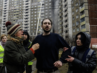 Local residents are reacting next to a burning residential high-rise building that has been damaged by a massive Russian missile strike in K...