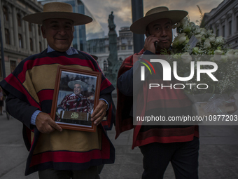 A pair of peasants are holding a picture of the former president and flowers as they attend the funeral of Sebastian Pinera in Santiago, Chi...