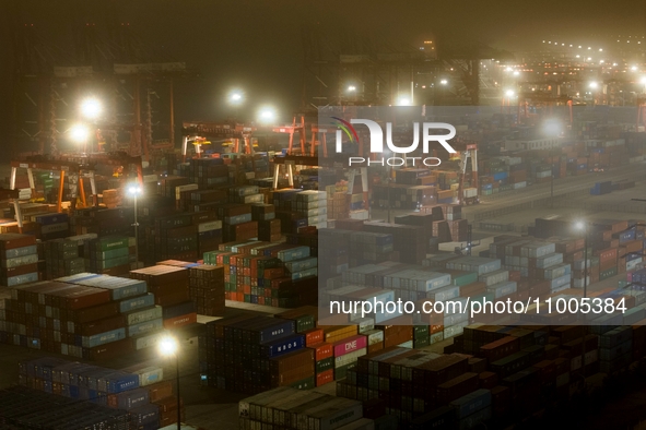 Vehicles are carrying containers to and from the Qianwan Container Terminal of Qingdao Port under heavy fog in Qingdao, China, on the evenin...