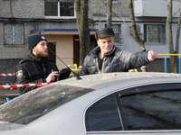A police officer and a senior man are standing by a car near a block of flats that was hit by a Russian Shahed drone during an overnight att...