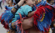 A man performing a pre-Hispanic dance is carrying his daughter in the Zocalo of Mexico Cit...