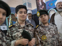 Young Iranian schoolboys in military uniforms are standing together in front of two clerics in the Imam Khomeini Grand Mosque during the 31s...
