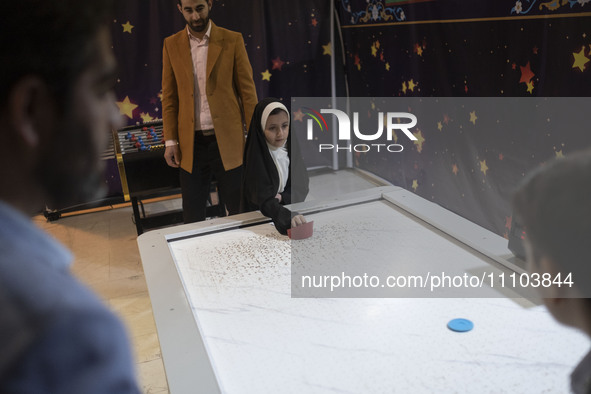 A young veiled Iranian girl is playing air hockey in the Imam Khomeini Grand Mosque at the 31st edition of the International Holy Quran Exhi...