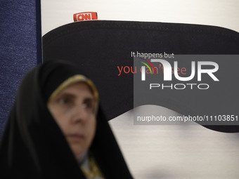 A veiled Iranian woman is standing in front of an anti-Western media poster at the Imam Khomeini Grand Mosque during the 31st edition of the...