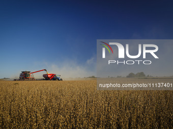 A combine is unloading grain onto a grain trailer while harvesting a soybean field. (