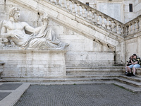 A couple is sitting on the steps next to the statue representing the river god Tevere (Tiber) in Rome, Italy, on April 14, 2024. Featuring 2...