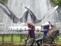 People and a rickshaw puller are crossing through a water fountain during an ongoing heatwave in Dhaka, Bangladesh, on April 20, 2024. (