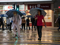 People are holding umbrellas while crossing the road in Hong Kong, on April 26, 2025. (