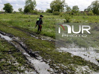 A boy is walking through puddles with a toy machine gun after rain on the road in a village in the Kyiv region, Ukraine, on April 25, 2024....