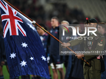 A member of the New Zealand Defence Force is holding the national flag of Australia during a pre-game ANZAC ceremony before the round ten Su...