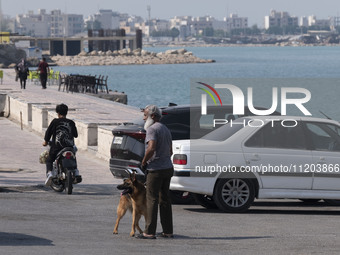 An Iranian man and his dog are standing on a coastal street in Bushehr, Iran, the country's first nuclear seaport city, located on the north...