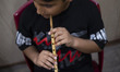 A young Iranian boy is playing a wooden flute while participating in a music class at an a...