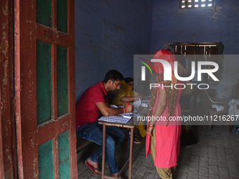 Election officials are checking the documents of a woman at a polling station during the third phase of the Indian General Elections in Hath...