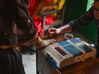 An election official is putting ink on the finger of a woman who is casting her vote at a polling station during the third phase of the Indi...