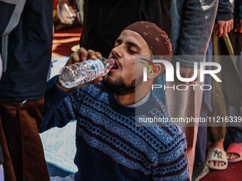 A Muslim boy is drinking water as he sits on the ground while others are donating blood during a blood donation camp in Sopore District, Bar...