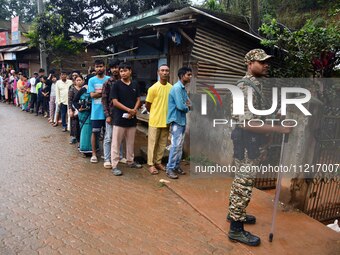 A security personnel is standing guard while voters are queuing to cast their ballots outside a polling station during the third phase of vo...