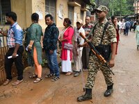 A security personnel is standing guard while voters are queuing to cast their ballots outside a polling station during the third phase of vo...