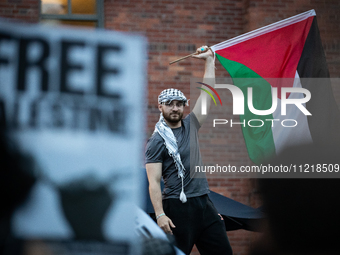 A demonstrator holds a Palestinian flag high as hundreds of people rally at the George Washington University Gaza solidarity encampment in r...