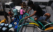 People are filling their water containers from a municipal water tanker outside a slum clu...