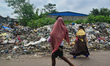 A couple is carrying their children while passing next to a garbage yard in Kolkata, India...