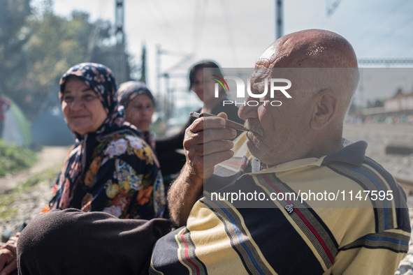 Old man smoking his pipe while her wife and daughters look at him, in Idomeni camp, on April 6 2016 