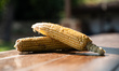 Two corns are lying on a wooden surface. 