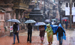 People with umbrellas walk around Patan Durbar Square, a UNESCO World Heritage Site in Lal...