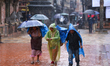 People with umbrellas walk around Patan Durbar Square, a UNESCO World Heritage Site in Lal...