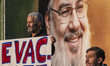 An elderly Iranian protester holds an anti-Israeli placard while standing in front of a gi...