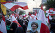 A veiled Iranian protester waves a Lebanese flag while standing behind a portrait of Leban...
