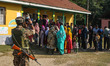 An Indian security personnel takes a picture of voters queuing to cast their ballots at a...