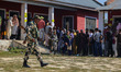 An Indian security personnel stands guard as voters queue to cast their ballots at a polli...