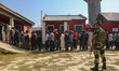 An Indian security personnel stands guard as voters queue to cast their ballots at a polli...