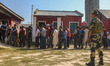 An Indian security personnel stands guard as voters queue to cast their ballots at a polli...
