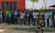 An Indian security personnel stands guard as voters queue to cast their ballots at a polli...