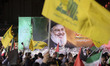 An Iranian man waves a flag of Lebanon's Hezbollah in front of a portrait of Lebanon's Hez...