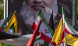 Iranian people wave flags in front of a portrait of Lebanon's Hezbollah Secretary General...