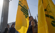 An Iranian man holds a flag of Lebanon's Hezbollah and a portrait of Hezbollah Secretary G...