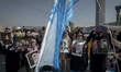 An Iranian man holds an Israeli flag while women and children hold portraits of Lebanon's...