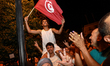 A young Tunisian on the shoulders of another young man waves the national flags of Tunisia...