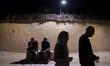Iranian youths walk past young men sitting on a path in Shiraz, Iran, on October 7, 2024,...