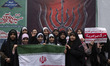 A group of veiled Iranian schoolgirls pose for a photograph while holding an Iranian flag...