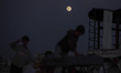 Palestinians walk along Salah al-Din Street as the full moon rises over the al-Bureij refu...