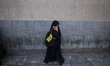 A veiled Iranian protester holds a flag of Lebanon's Hezbollah while standing on a sidewal...