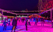 Families and people of all ages ice skate surrounded by vibrant lights and decorations in...