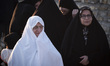 An elderly Iranian woman wearing a white veil stands with her family in a tourism camp in...
