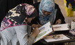 Two young female Iranian Islamic fashion designers work as they sit at a stand dedicated t...